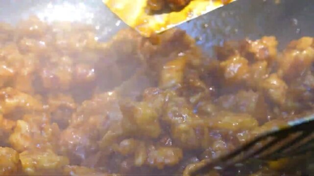 A high-definition, steaming close-up shot capturing golden, crispy battered chicken pieces being tossed and glazed in a rich, glossy orange sauce.