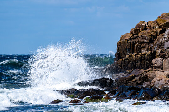 Powerful wave crashing against dark rocky coastal cliffs