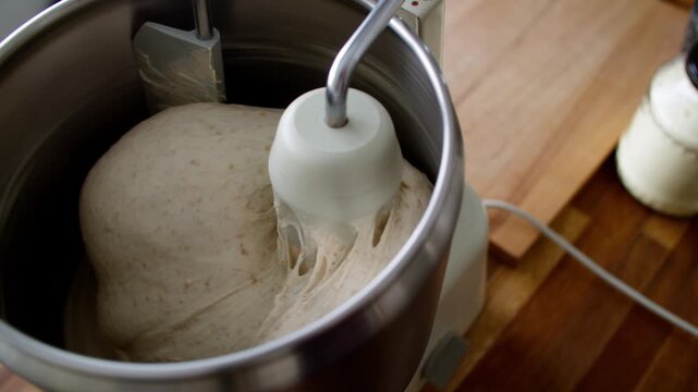 Bread dough being kneaded in robust home stand mixer; slow camera push in. 