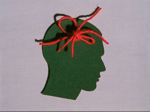 Green felt head silhouette with tangled red thread on a textured white background for mental health and anxiety awareness campaigns