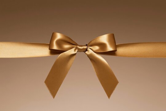 Gold satin bow and ribbon on a warm tan background, featuring soft woven textures and a luxurious sheen for festive headers and gift mockup designs