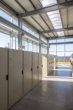Modern storage facility interior featuring rows of beige lockers with green indicators, large windows allowing natural light and solar panels visible outside