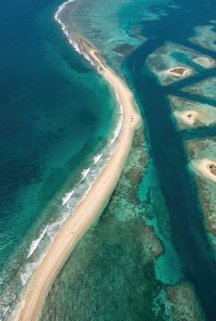Aerial view of a sandy beach curving into turquoise waters, surrounded by coral reefs and small islands, showcasing a vibrant coastal landscape