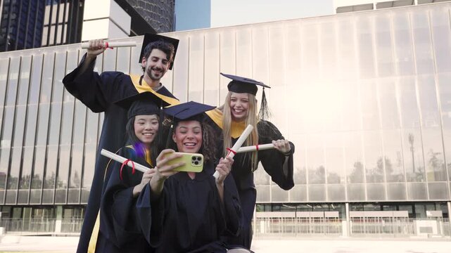 Happy multiethnic graduate students taking a selfie with a smartphone. University graduates celebrating with diplomas