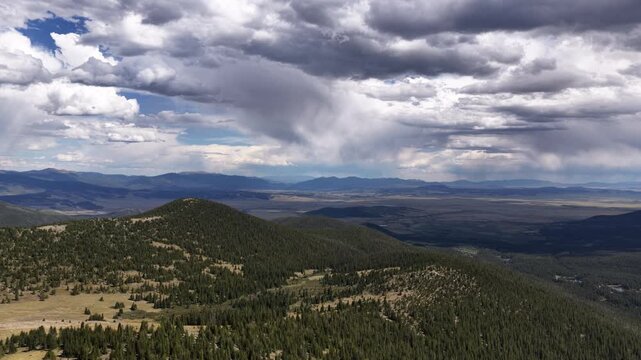 Aerial of forested mountains and meadows under dramatic cloudy sky in Colorado near Keystone