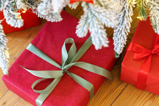 Beautiful presents, gift boxes wrapped in elegant red paper under green snowy festive Christmas tree with warm lights. Cozy winter holiday atmosphere perfect for seasonal celebrations and decor themes