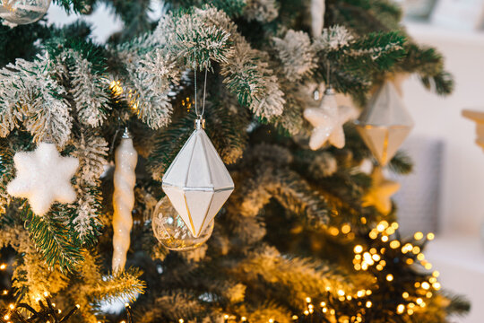 Close up of frosted Christmas tree branch decorated with white ornaments, stars, icicles and warm glowing lights, creating a cozy festive atmosphere. Holiday mood, aesthetic decor