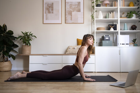 Woman doing cobra pose yoga watching laptop online