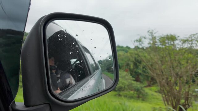 Car wing mirror reflecting a green countryside road trip