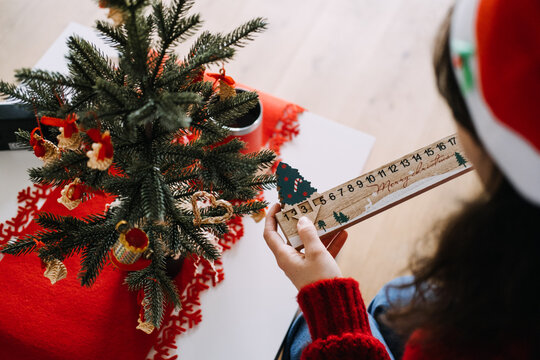 Woman in Santa hat holds wooden advent countdown board with MERRY CHRISTMAS text beside decorated miniature tree. marking days until christmas, reusable advent calendar, minimalist countdown decor