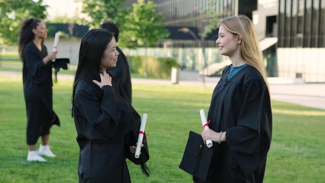 Female graduates in gowns and caps conversing and smiling together after the university graduation ceremony