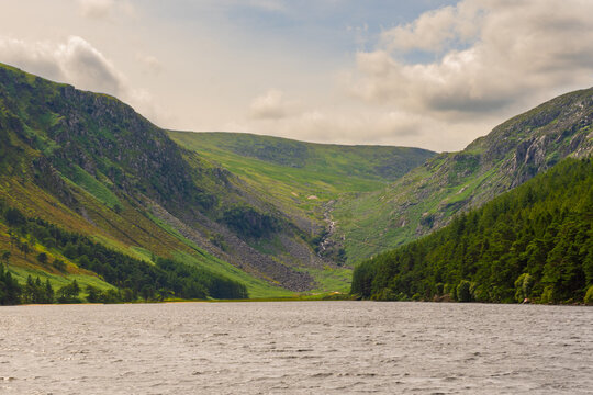 Serene lake reflects calm sky above rugged green hills