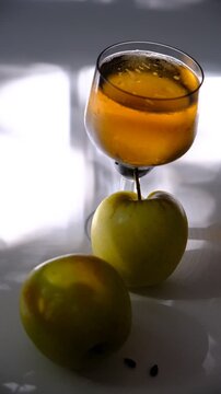 Glass of brut apple cider from Normandy with ripe yellow fruits on a white table. Atmospheric still life featuring a glass of brut apple cider from Normandy on a white table. 