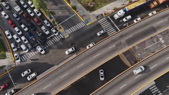 High aerial view of a busy city intersection and highway overpass with traffic queueing at a red light
