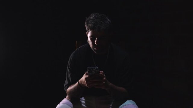 Man Scrolling Smartphone Alone in Dark Room