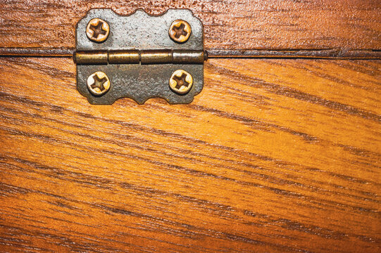 Close-up of vintage brass hinge on honey-colored wooden surface