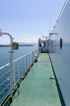 low-angle shot along the turquoise green deck and white bulkhead of a moving car ferry on clear blue sea water, under a bright, sunny sky