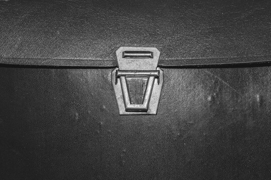 Black and white metal suitcase latch on dark leather texture