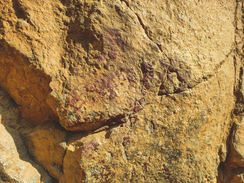 Rough ochre rock surface with deep cracks and red mineral stains