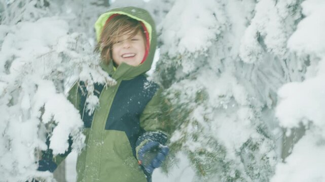 Toddler in a green hooded jacket walking among snowy trees shot from behind in soft focus