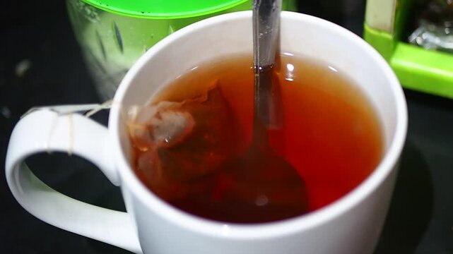 Close-up of a spoon stirring a teabag in a white ceramic mug of hot, freshly brewed tea.