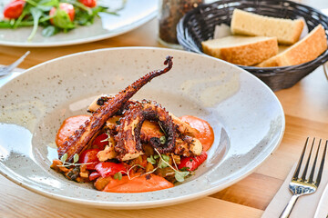 Grilled octopus dish served with vegetables and bread on wooden table © Elizaveta