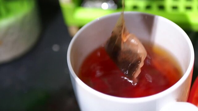 Close-up of a hand dipping a tea bag into a white mug with hot, steaming tea, brewing a warm beverage for a morning drink