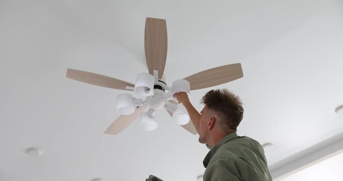 Man replacing light bulb in ceiling fan at home, low angle view