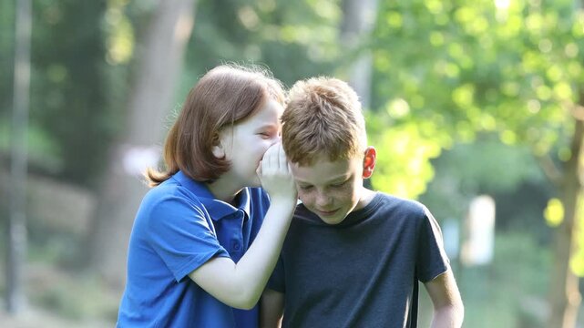 Little boy whispering something to his friend in park at summer