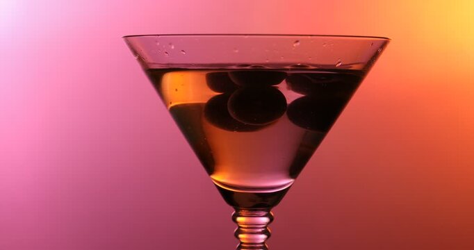 Olives falling into martini glass with cocktail on color background, closeup