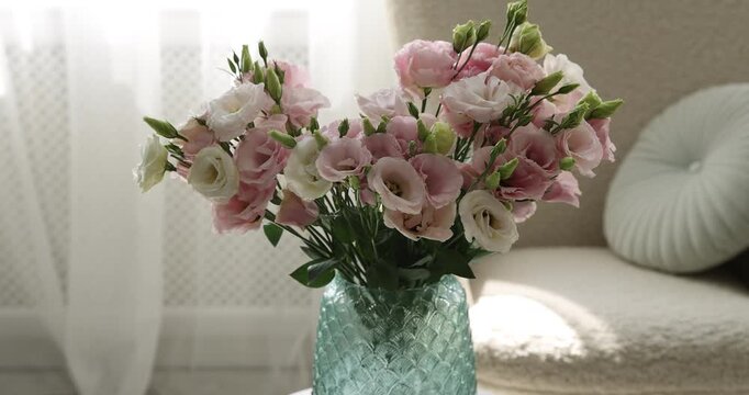 Bouquet of beautiful eustoma flowers in vase on white coffee table indoors, closeup. Camera moving forward