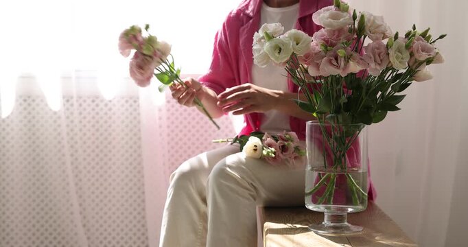 Woman putting beautiful eustoma flowers into vase on bench indoors, closeup. Space for text