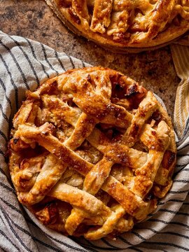 Top down flat lay view of a freshly baked golden apple pie with a lattice crust resting on a striped kitchen towel.