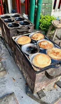 High angle view of traditional Indonesian serabi pancakes cooking in a classic metal mold over a stove outdoors.
