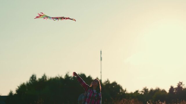 Woman flying a colorful kite in a park as it rises, glides, and dips against the evening sky. Outdoor recreation and carefree summer concept