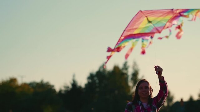 Woman flying a colorful kite in a park as it rises, glides, and dips against the evening sky. Outdoor recreation and carefree summer concept