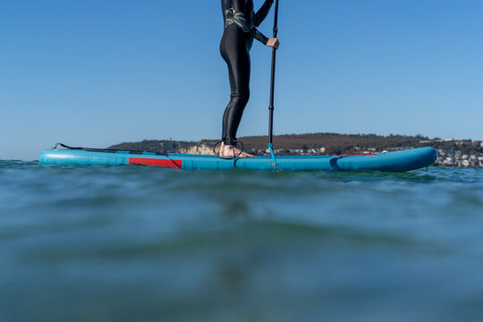 Woman stand-up paddle boarding on calm ocean water under clear sky