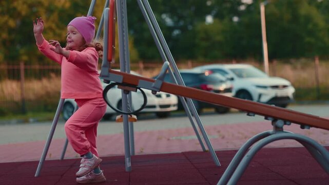 Girl playing on a playground seesaw, balancing and walking around outdoor equipment during active childhood recreation