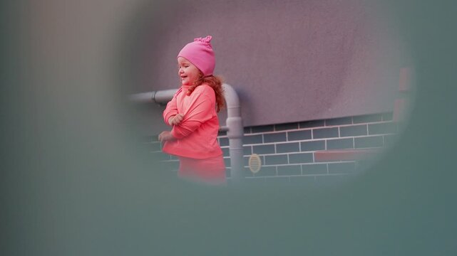 Young girl in pink clothing walking past a tiled wall and bench, candid outdoor movement sequence with playful childhood lifestyle concept