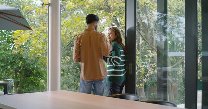 Couple by glass door, African man entering with smartphone, embracing woman, watching backyard