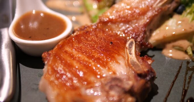 Close up of grilled juicy pork chop steak with brown gravy sauce in restaurant