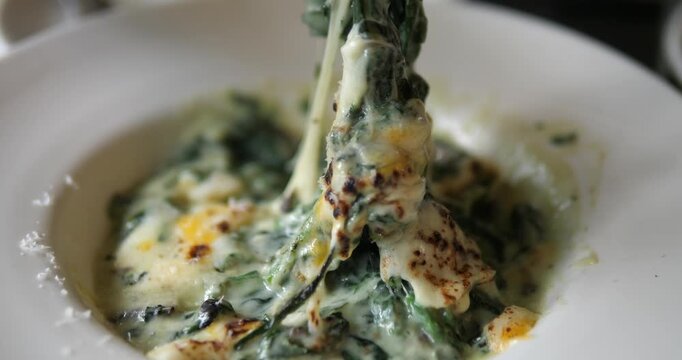 Close up of fork lifting hot baked spinach with stretchy melted mozzarella cheese pull