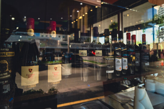 Close-up of the Escudo Rojo, J. Lohr, Pergola, and Kvint Kosher Merlot wine bottles on the display shelf behind the store's glass window. Sunny Isles Beach, FL, USA - August 8 2026