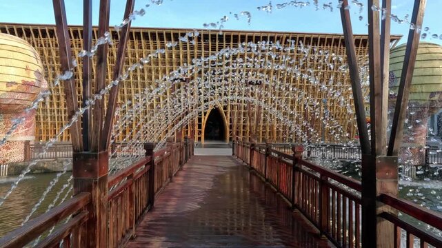 A beautiful wooden bridge features a unique arch-shaped fountain with water droplets forming a patterned arch.