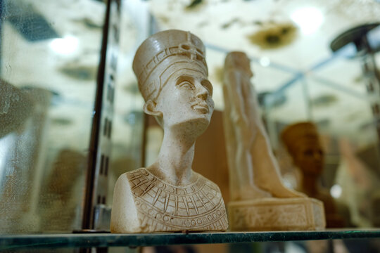 White stone bust sculpture of Nefertiti displayed on a glass shelf inside a curio shop