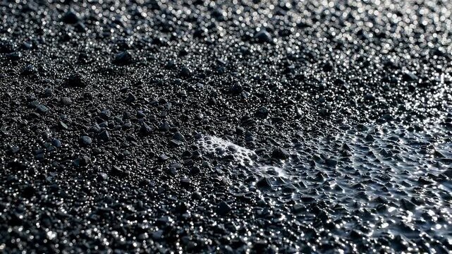 Wet black asphalt surface texture with glistening rain drops and water reflection in macro detail