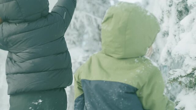 Two boys walking together through snow-covered trees seen from behind in a winter park