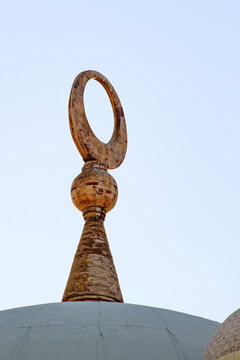 Close up of a traditional crescent moon finial atop a dome against a pale sky