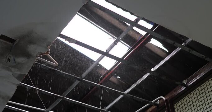 Severe ceiling collapse with heavy rainwater pouring through broken roof