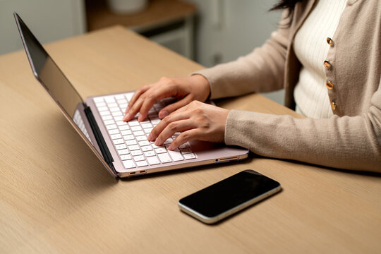 Woman typing on laptop with smartphone nearby in modern home office workspace